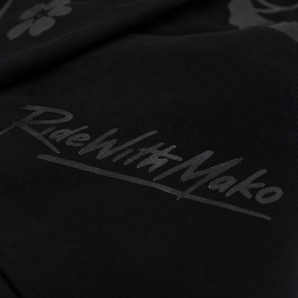 Close-up of a black fabric product featuring a tonal dark gray 'RideWithMako' script logo and a subtle floral pattern.